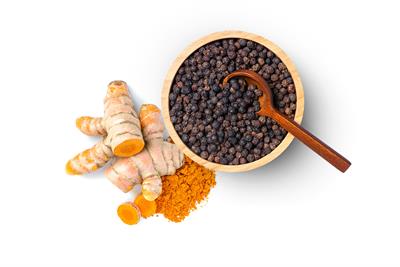 Black peppercorns in a bowl next to turmeric root